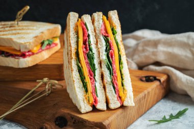 Two homemade sandwiches with sausage, cheese and arugula on a light concrete background. The concept of a quick meal or snack at work or school.