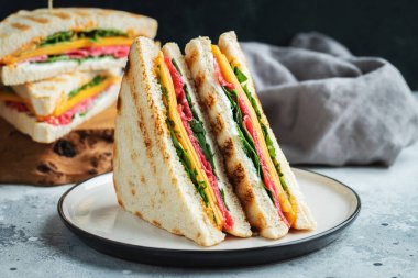 Two homemade sandwiches with sausage, cheese and arugula on a light concrete background. The concept of a quick meal or snack at work or school.
