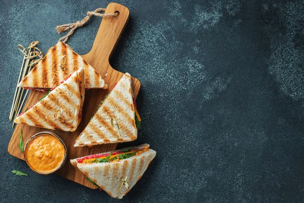 Four homemade sandwiches with sausage, cheese and arugula on a dark concrete background. The concept of a quick meal or snack at work or school. Top view with copy space
