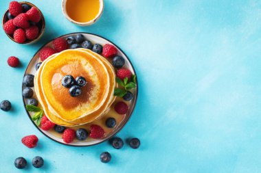 Close-up delicious pancakes, with fresh blueberries, raspberry and maple syrup or honey on a light background. Top view with copy space.