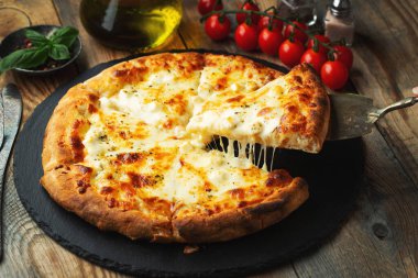 A slice of hot Italian pizza with stretching cheese. Pizza four cheeses with basil on a wooden background.