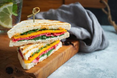 Two homemade sandwiches with sausage, cheese and arugula on a light concrete background. The concept of a quick meal or snack at work or school.