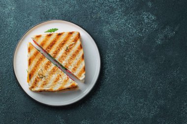Two homemade sandwiches with sausage, cheese and arugula on a dark concrete background. The concept of a quick meal or snack at work or school. Top view with copy space