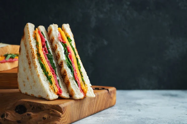 Two homemade sandwiches with sausage, cheese and arugula on a light concrete background. The concept of a quick meal or snack at work or school. With copy space