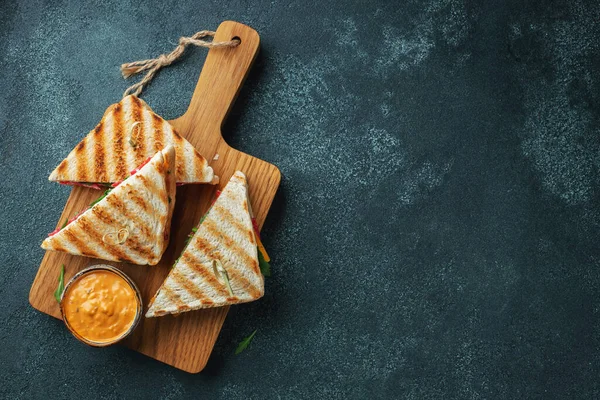 Four homemade sandwiches with sausage, cheese and arugula on a dark concrete background. The concept of a quick meal or snack at work or school. Top view with copy space