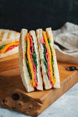 Two homemade sandwiches with sausage, cheese and arugula on a light concrete background. The concept of a quick meal or snack at work or school.