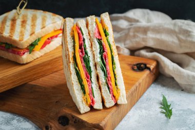 Two homemade sandwiches with sausage, cheese and arugula on a light concrete background. The concept of a quick meal or snack at work or school. With copy space