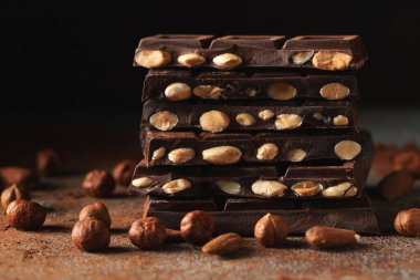 Dark and milk chocolate with nuts on a dark background sprinkled with cocoa powder. Chocolate pieces with almonds and hazelnuts close-up. With copy space