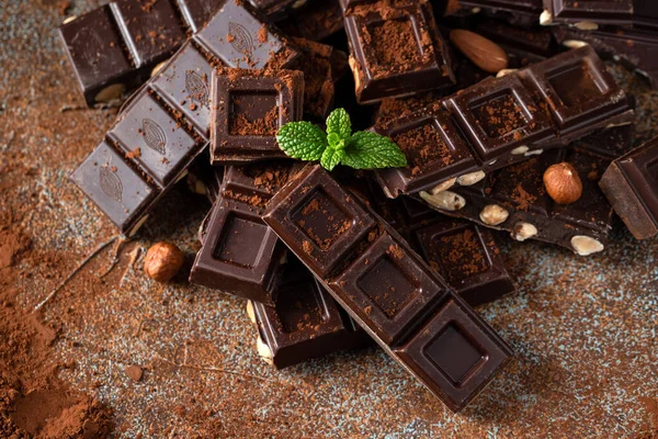 stock image Dark and milk chocolate with nuts on a dark background sprinkled with cocoa powder. Chocolate pieces with almonds and hazelnuts close-up. Top view