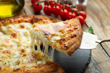A slice of hot Italian pizza with stretching cheese. Pizza four cheeses with basil on a wooden background.