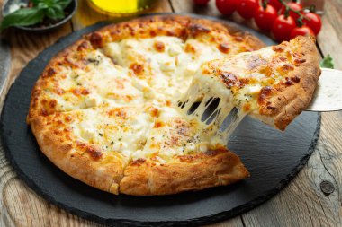 A slice of hot Italian pizza with stretching cheese. Pizza four cheeses with basil on a wooden background.