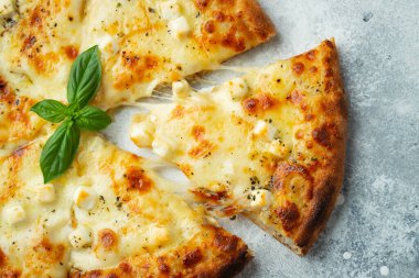 Italian pizza four cheeses with stretching cheese and basil on a light concrete background.