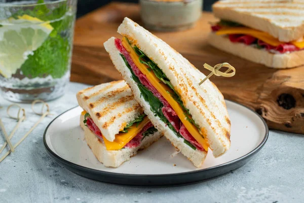 Two homemade sandwiches with sausage, cheese and arugula on a light concrete background. The concept of a quick meal or snack at work or school.