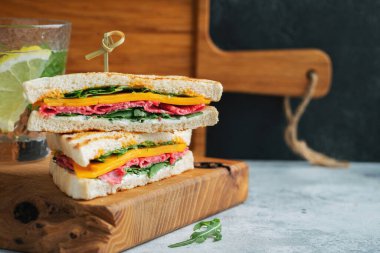 Two homemade sandwiches with sausage, cheese and arugula on a light concrete background. The concept of a quick meal or snack at work or school. With copy space