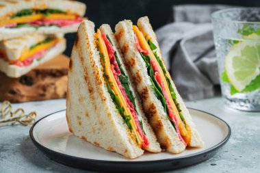 Two homemade sandwiches with sausage, cheese and arugula on a light concrete background. The concept of a quick meal or snack at work or school.