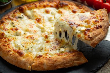 A slice of hot Italian pizza with stretching cheese. Pizza four cheeses with basil on a wooden background.
