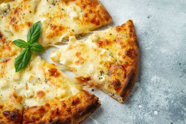 Italian pizza four cheeses with stretching cheese and basil on a light concrete background.