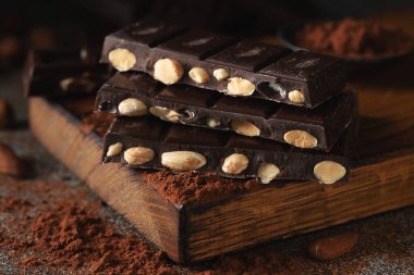 Dark and milk chocolate with nuts on a dark background sprinkled with cocoa powder. Chocolate pieces with almonds and hazelnuts close-up.