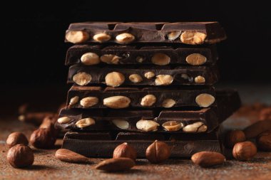 Dark and milk chocolate with nuts on a dark background sprinkled with cocoa powder. Chocolate pieces with almonds and hazelnuts close-up.