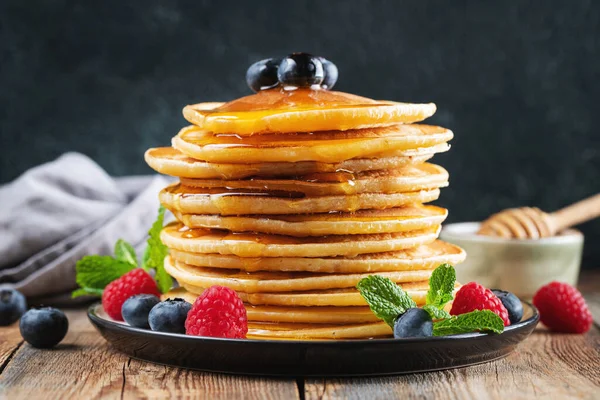 stock image Close-up delicious pancakes, with fresh blueberries, raspberry and maple syrup or honey on a dark background. Sweet maple syrup flows from a stack of pancake