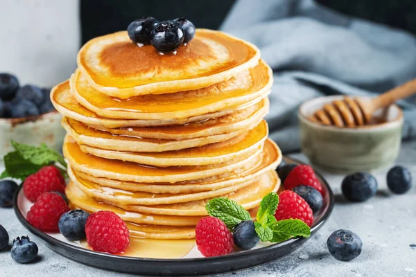 stock image Close-up delicious pancakes, with fresh blueberries, raspberry and maple syrup or honey on a dark background. Sweet maple syrup flows from a stack of pancake