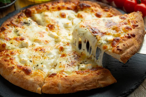 A slice of hot Italian pizza with stretching cheese. Pizza four cheeses with basil on a wooden background.
