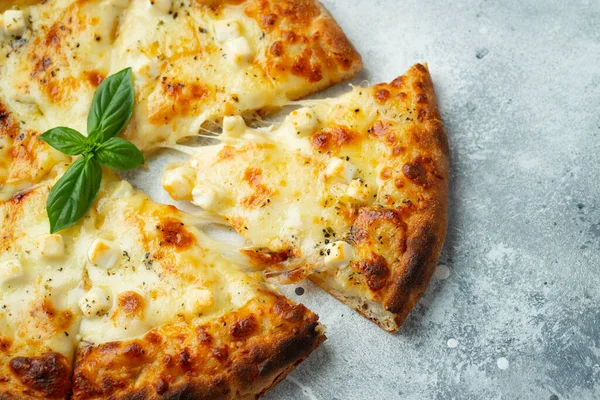 Italian pizza four cheeses with stretching cheese and basil on a light concrete background.