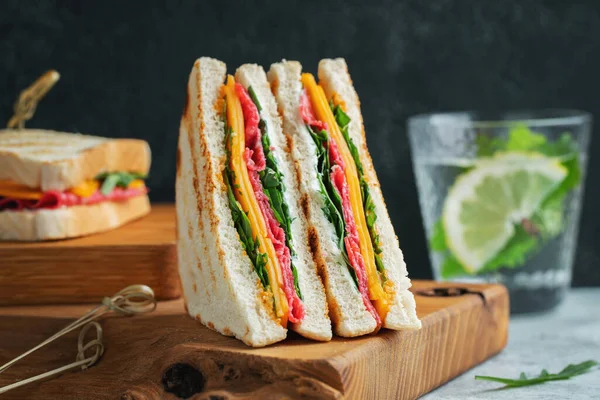 Two homemade sandwiches with sausage, cheese and arugula on a light concrete background. The concept of a quick meal or snack at work or school.