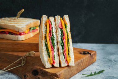Two homemade sandwiches with sausage, cheese and arugula on a light concrete background. The concept of a quick meal or snack at work or school. With copy space