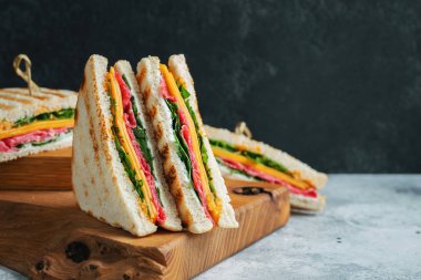 Two homemade sandwiches with sausage, cheese and arugula on a light concrete background. The concept of a quick meal or snack at work or school. With copy space