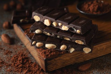 Dark and milk chocolate with nuts on a dark background sprinkled with cocoa powder. Chocolate pieces with almonds and hazelnuts close-up.