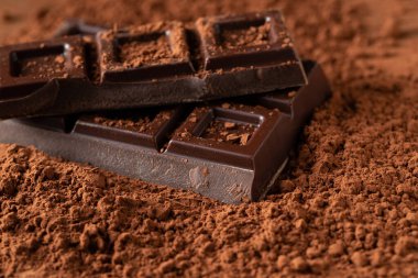 Dark and milk chocolate with nuts on a dark background sprinkled with cocoa powder. Chocolate pieces with almonds and hazelnuts close-up. Top view with copy space.