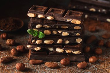 Dark and milk chocolate with nuts on a dark background sprinkled with cocoa powder. Chocolate pieces with almonds and hazelnuts close-up.