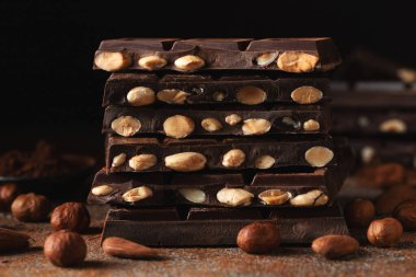 Dark and milk chocolate with nuts on a dark background sprinkled with cocoa powder. Chocolate pieces with almonds and hazelnuts close-up.