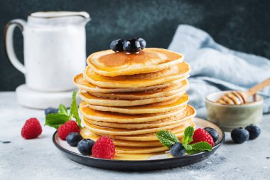 Close-up delicious pancakes, with fresh blueberries, raspberry and maple syrup or honey on a dark background. Sweet maple syrup flows from a stack of pancake