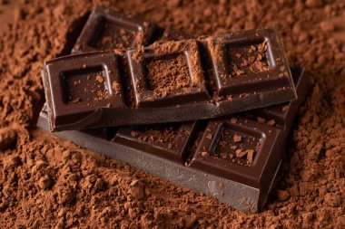Dark and milk chocolate with nuts on a dark background sprinkled with cocoa powder. Chocolate pieces with almonds and hazelnuts close-up. Top view with copy space.