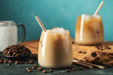Krema dökülmüş uzun bir bardakta buzlu kahve. Koyu beton bir masada buz küpleri ve fasulyeler. Siyah arka planda fotokopi alanı olan soğuk yaz içecekleri..
