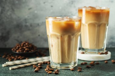 Krema dökülmüş uzun bir bardakta buzlu kahve. Koyu beton bir masada buz küpleri ve fasulyeler. Siyah arka planda fotokopi alanı olan soğuk yaz içecekleri..