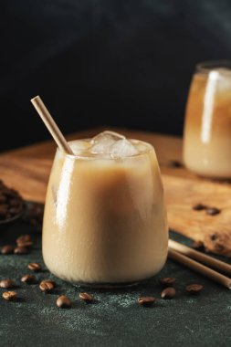 Krema dökülmüş uzun bir bardakta buzlu kahve. Koyu beton bir masada buz küpleri ve fasulyeler. Siyah arka planda fotokopi alanı olan soğuk yaz içecekleri..