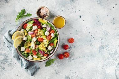Farklı yaprak ve sebzelerden oluşan lezzetli ve sağlıklı yeşil salata. Hafif beton arka planda tohum ve peynir karışımı. Boşluğun bir kopyasıyla en üstteki görünüm.