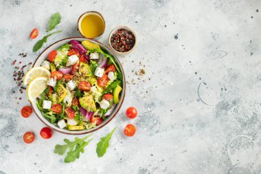 Farklı yaprak ve sebzelerden oluşan lezzetli ve sağlıklı yeşil salata. Hafif beton arka planda tohum ve peynir karışımı. Boşluğun bir kopyasıyla en üstteki görünüm.