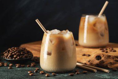 Krema dökülmüş uzun bir bardakta buzlu kahve. Koyu beton bir masada buz küpleri ve fasulyeler. Siyah arka planda fotokopi alanı olan soğuk yaz içecekleri..
