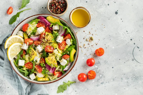 Farklı yaprak ve sebzelerden oluşan lezzetli ve sağlıklı yeşil salata. Hafif beton arka planda tohum ve peynir karışımı. Boşluğun bir kopyasıyla en üstteki görünüm.
