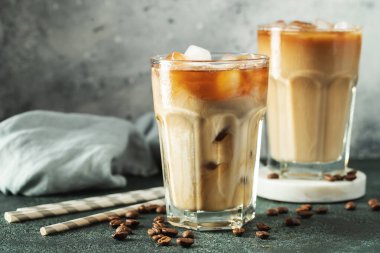 Krema dökülmüş uzun bir bardakta buzlu kahve. Koyu beton bir masada buz küpleri ve fasulyeler. Siyah arka planda fotokopi alanı olan soğuk yaz içecekleri..