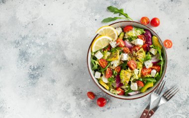 Farklı yaprak ve sebzelerden oluşan lezzetli ve sağlıklı yeşil salata. Hafif beton arka planda tohum ve peynir karışımı. Boşluğun bir kopyasıyla en üstteki görünüm.