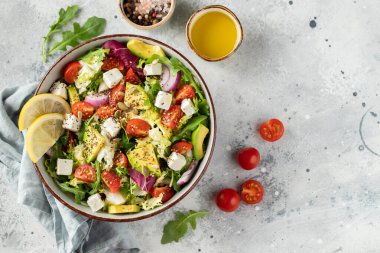 Farklı yaprak ve sebzelerden oluşan lezzetli ve sağlıklı yeşil salata. Hafif beton arka planda tohum ve peynir karışımı. Boşluğun bir kopyasıyla en üstteki görünüm.