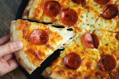 Bir dilim peynirli sıcak İtalyan pizzası. Koyu ahşap arka planda pizza sosisi..