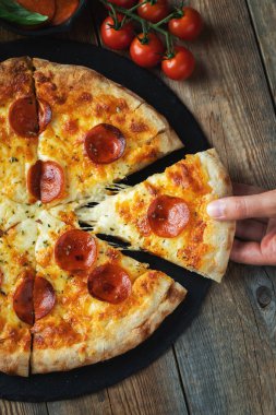 Bir dilim peynirli sıcak İtalyan pizzası. Koyu ahşap arka planda pizza sosisi..