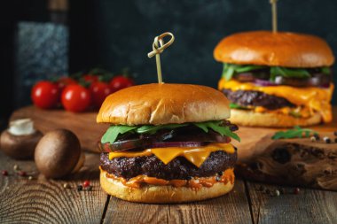 Eski ahşap bir masada iki lezzetli ev yapımı sığır eti, peynir ve mantar burger. Yağlı, sağlıksız yiyecekler..