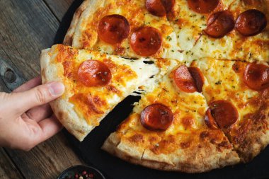 Bir dilim peynirli sıcak İtalyan pizzası. Koyu ahşap arka planda pizza sosisi..